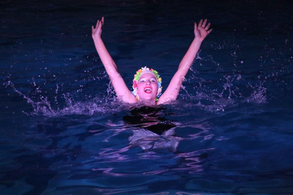 Freshman Kate Nowak smiles at the crowd before sinking into the water during the freshman class dance routine. It is a tradition for the freshman cuties to wear the flowered swim caps during their class dance.